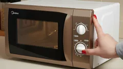 Žena nastavuje mikrovlnnú rúru na ohrev jedla v kuchyni.